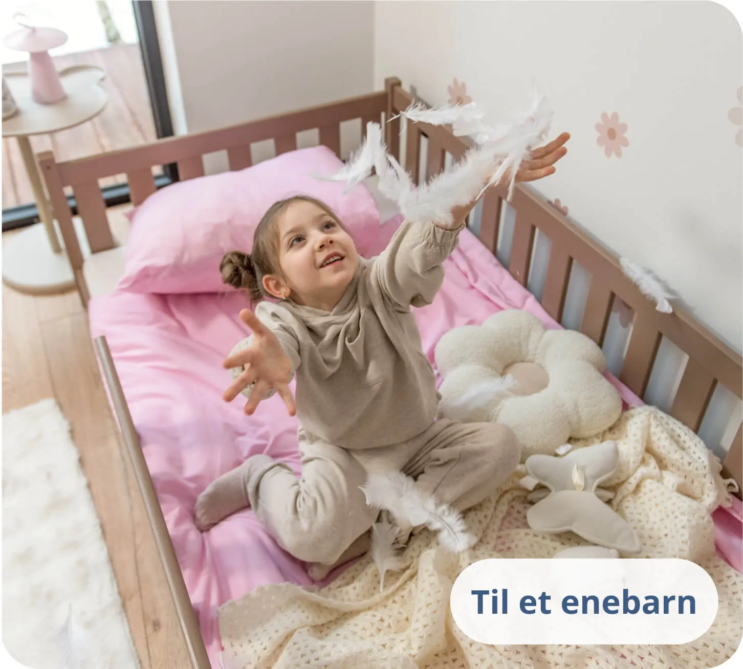 Pige leger med hvide fjer på lyserødt sengetøj i en chokoladefarvet seng.